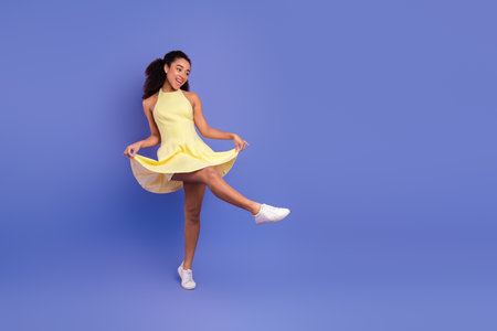 Cheerful young woman in a yellow dress posing playfully against a purple background, expressing happiness and vibrant style.の写真素材