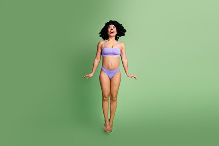 Charming woman with natural beauty poses gracefully, celebrating body positivity on a green background in purple lingerieの写真素材