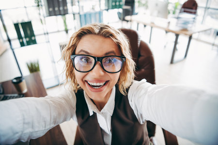 Businesswoman in glasses working at a modern office desk, smiling with confidence and charmの写真素材