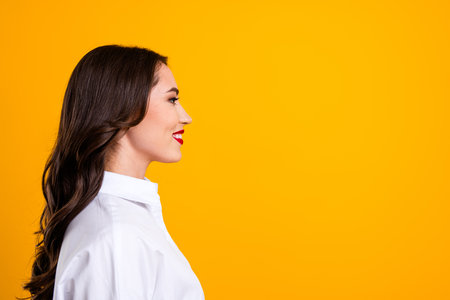 Side profile of a stylish brunette woman in a white shirt set against a vibrant yellow background, radiating confidenceの写真素材