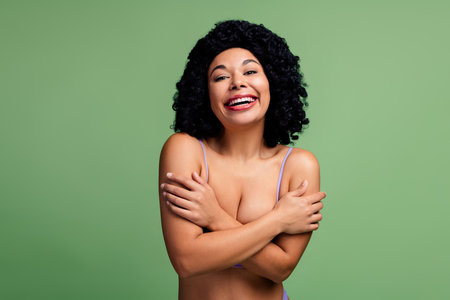 Confident young woman with natural curls embracing herself expresses self-love on a green backgroundの写真素材