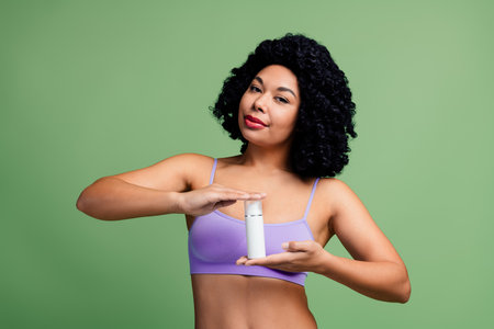 Confident Woman Displaying Skincare Product Against a Green Background Promoting Natural Beauty and Self-Careの写真素材