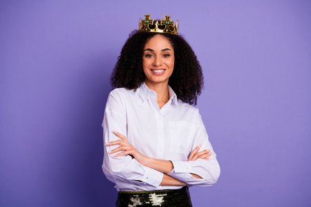 Confident woman wearing a crown and white shirt, exuding elegance and authority, standing against a...