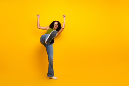 African American woman posing with enthusiasm and energy against a vivid yellow background in casual green top and stylish jeansの写真素材