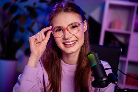 Young female vlogger smiling while recording content with microphone in modern setup with vibrant neon lightingの写真素材