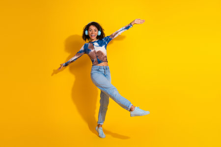 Joyful young woman posing energetically against a vibrant yellow background, expressing happiness...