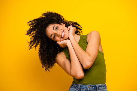 Young stylish woman with curly hair posing against a yellow background wearing casual green top and denim jeansの写真素材
