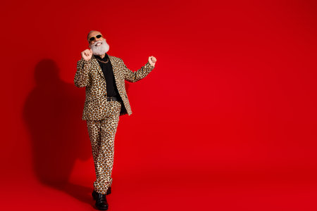 Elderly gentleman in a leopard print suit dancing confidently against a vibrant red backgroundの写真素材
