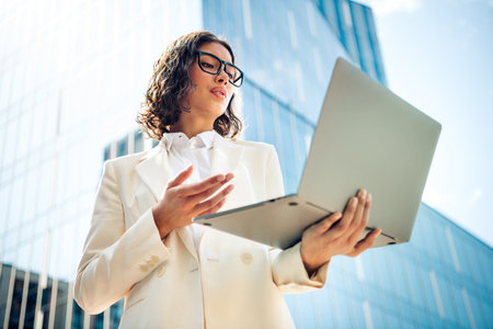 Successful young businesswoman working outdoors on a sunny day with a laptop, demonstrating professional successの写真素材