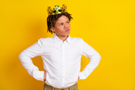 Confident young boy wearing a crown posing against a vibrant yellow background showcasing determination and styleの写真素材