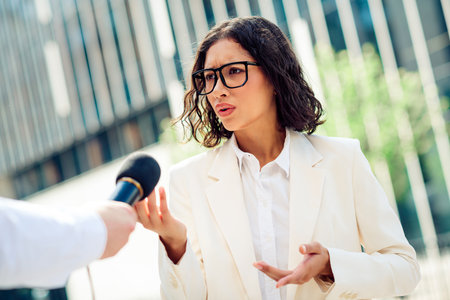 Confident businesswoman speaking outdoors in professional attire during an urban interview settingの写真素材