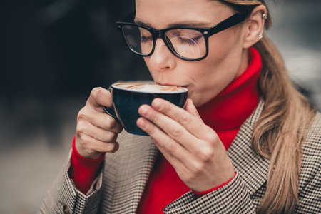Charming woman enjoying a coffee outdoors while dressed elegantly for a business occasion during a...