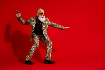 Charming elderly man in leopard suit posing with playful gestures on a vibrant red background, exuding charismaの写真素材