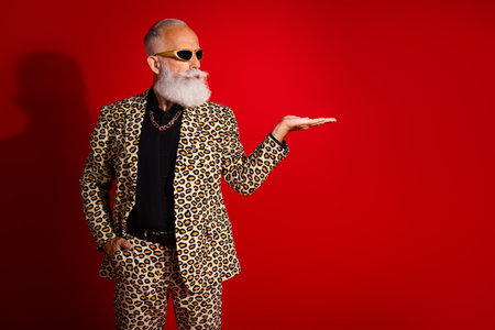 Fashionable elderly man in leopard suit making gesture on bold red backdrop showcasing eclectic fashion and jubilant personaの写真素材