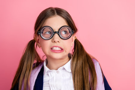Portrait of a cheerful schoolgirl with glasses and ponytails posing in a stylish school uniform on a...