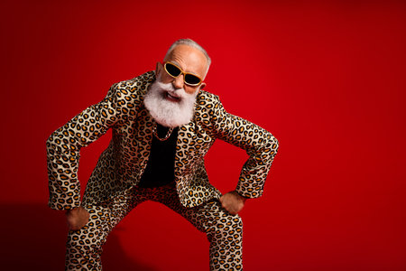 Stylish gentleman wearing leopard-print suit and sunglass posing energetically against a vibrant red backgroundの写真素材