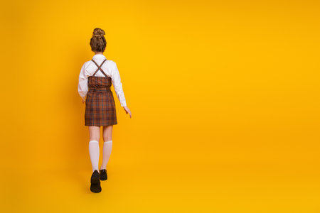 Young female student standing stylishly posed on a vivid yellow background, promoting education and youthful energyの写真素材
