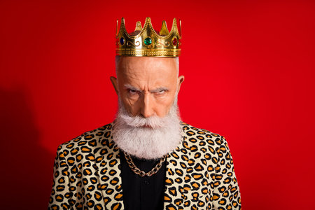 Senior man in leopard print jacket wearing a crown against a red backdrop, showcasing eccentric charm, fashionable styleの写真素材