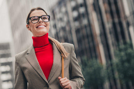 Young businesswoman with glasses in formalwear walking outdoors in urban setting under daylightの写真素材