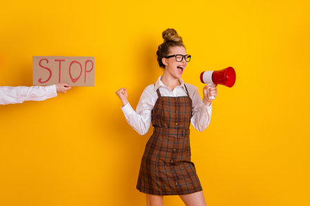 Confident young woman with megaphone promoting ideas against yellow background, emphasizing...