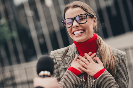 Smiling female professional wearing glasses and formal attire in an urban business setting during an interviewの写真素材