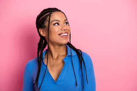 Charming young woman with braided hair in a blue shirt smiling against a vibrant pink background, exuding positivity and style.の写真素材