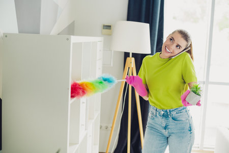 Young woman multitasking cleaning and chatting happily in a cozy living room interior with modern decor and sunlightの写真素材