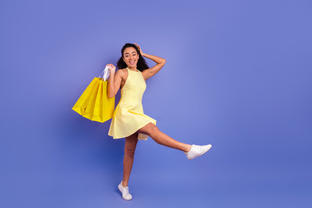 Young woman with yellow shopping bags poses joyfully on purple background in a stylish summer dressの写真素材