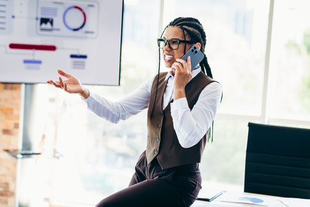 Successful businesswoman engaged in a phone call while presenting office data during a professional...