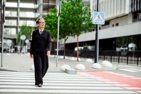 Successful businesswoman crossing an urban street in formalwear, showcasing confidence and elegance in a modern city workplaceの写真素材