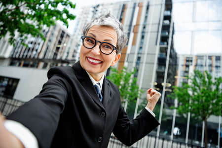 Cheerful professional woman celebrating success outdoors in urban business environmentの写真素材