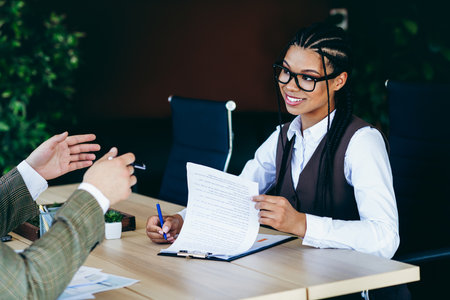 Businesswoman reviewing documents with a colleague in a professional office setting, showcasing teamwork and focusの写真素材