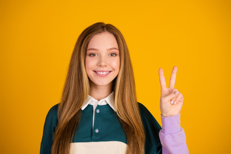 Cute woman in casual fashion on a yellow background posing with a peace gesture, representing...