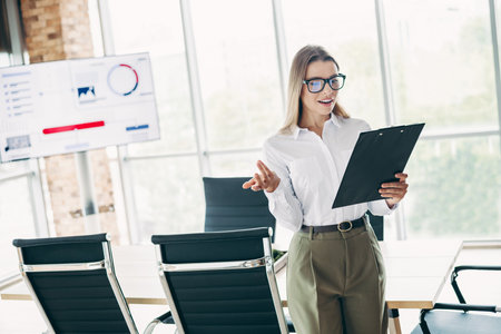 Confident businesswoman presenting financial data in modern office workspace with visual aids and professional attireの写真素材
