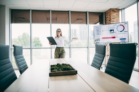 Professional businesswoman presenting data analysis in a modern office setting during a corporate meetingの写真素材