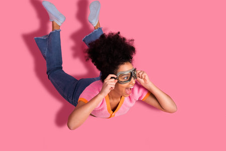 Cheerful girl enjoying imaginative adventure wearing goggles on a vibrant pink background for a...