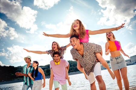 Group of cheerful friends enjoying a sunny day outdoors near a waterfront, celebrating youth and...