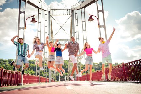 Group of joyful young friends jumping on a bridge during a bright summer day celebrating happiness and funの写真素材