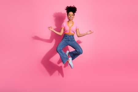 Young cheerful woman meditating in midair against pink background wearing casual stylish outfit with...