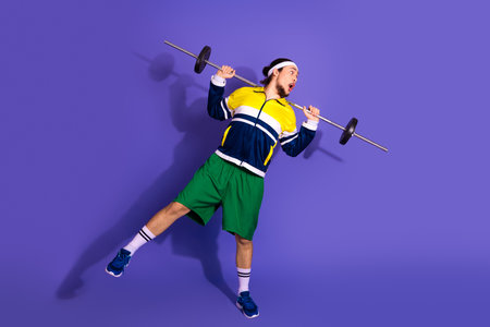 Young athletic man in retro sportswear energetically lifting weights in front of a vibrant purple...