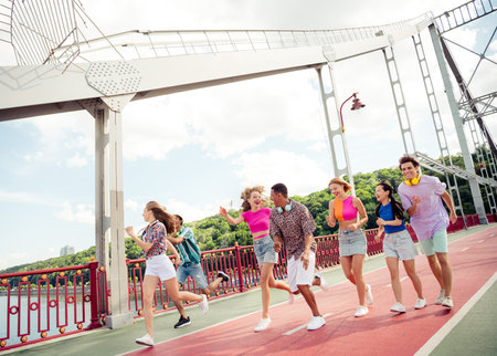 Group of cheerful young friends having fun outdoors on an urban bridge on a bright sunny day