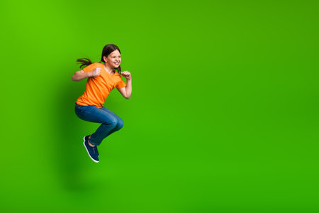 Cheerful preteen girl in bright outfit jumping against green background, symbolizing happiness,...