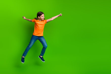 Excited young girl jumping enthusiastically in casual clothes with a vibrant green background...