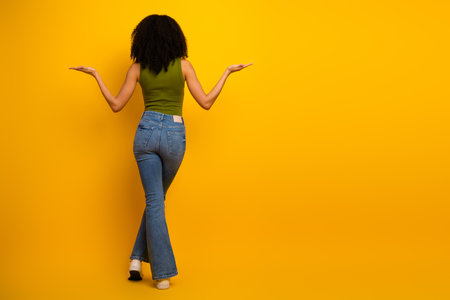Young woman in stylish casual outfit stands against vibrant yellow background, showcasing fashionの写真素材