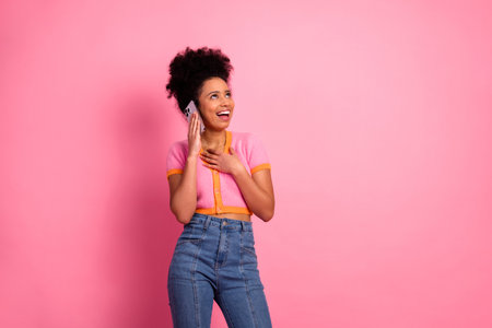 Cheerful girl on phone expressing excitement against a pink background, wearing casual trendy style representing leisureの写真素材