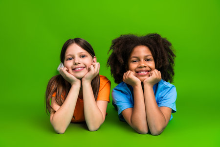 Happy young girls lying on a green background smiling, symbolizing friendship and joy, showcasing togetherness and diversityの写真素材