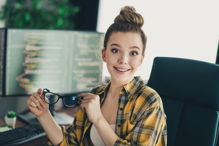 Young female programmer in casual attire sitting at workplace with computers in the background...