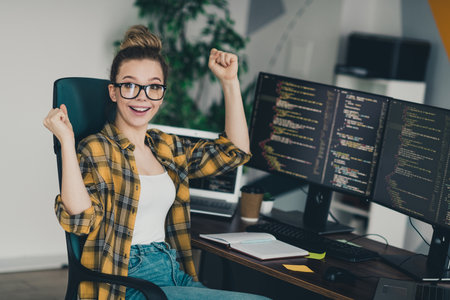 Excited female programmer celebrating success while coding at her desk in a modern workspace during workの写真素材
