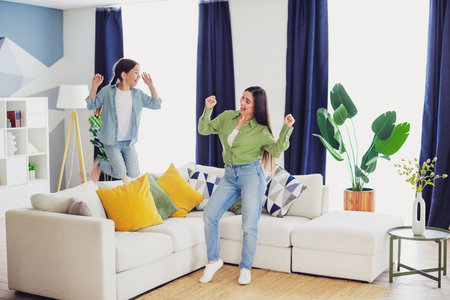 Mother and daughter dancing together in a bright living room, celebrating a joyful family moment in a casual and stylish homeの写真素材