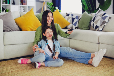 Mother and daughter sitting together on a cozy sofa enjoying leisure in a stylish home interior with colorful cushionsの写真素材